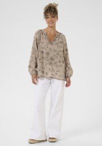 Bluză florală bej cu decolteu în V și manșete strânse, asortată cu pantaloni albi cu picioare largi și sandale espadrile cu platformă.