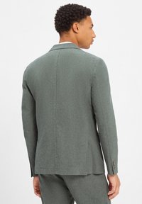 Op maat gemaakte grijze blazer, gestructureerde stof, notch kraag, enkele achteropening, knopenmanchetten, slim fit en achternaad details.