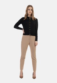 Cardigan nero con bottoni dorati, abbinato a pantaloni beige su misura e tacchi con stampa leopardata, caratterizzato da un design slim fit.