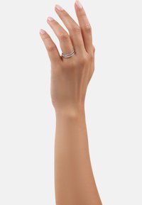 Main droite avec des ongles rose clair portant une bague argentée à double bande avec de petites pierres incrustées sur le majeur.