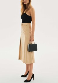 Czarny prążkowany body, beżowa spódnica midi z przednim rozcięciem, czarna torebka z metalowymi akcentami oraz czarne zamszowe szpilki.
