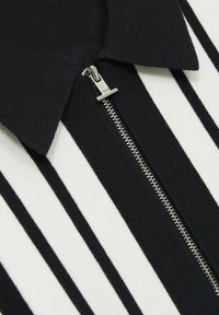 Polo cu dungi alb-negru, cu închidere prin fermoar și guler ribot, având un fermoar argintiu și un material texturat.