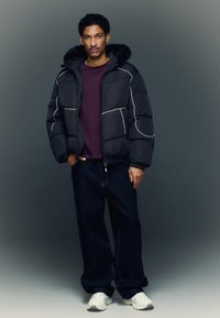 Musta untuvatakki valkoisilla saumuksilla, turkiskaulus, yhdistetty viininpunaiseen collegepaitaan ja tummiin farkkuihin. Mallilla on valkoiset lenkkarit.