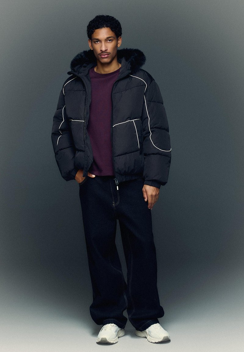 Musta untuvatakki valkoisilla saumuksilla, turkiskaulus, yhdistetty viininpunaiseen collegepaitaan ja tummiin farkkuihin. Mallilla on valkoiset lenkkarit.