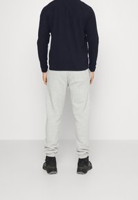 Marinblå långärmad skjorta i kombination med ljusgråa sweatpants som har elastiska muddar, samt svarta sportskor med texturerade sulor.