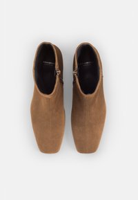 Botas de tobillo de gamuza marrón con una textura suave, que cuentan con un cierre de cremallera lateral y un diseño elegante y puntiagudo.