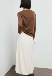 Brun langærmet sweater parret med en creamfarvet maxi-nederdel. Sweateren har en glat tekstur; nederdelen er let og når anklerne.
