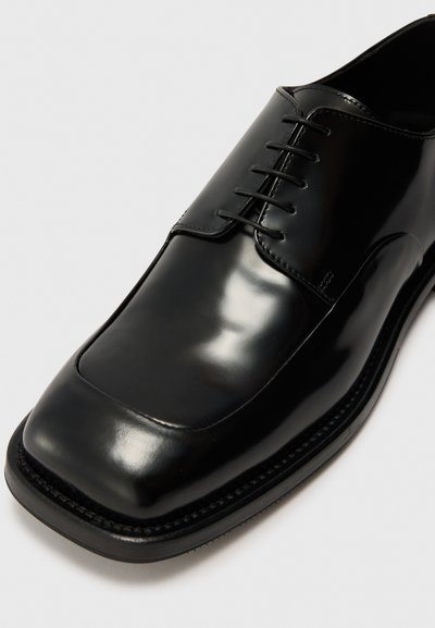 Black leather dress shoe with a polished finish, square toe, and four eyelets. Features black laces and a textured black outsole.
