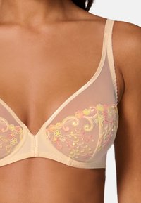 Beige bra with sheer cups featuring multicolored floral embroidery, triangular shape, and adjustable straps. Smooth fabric texture.