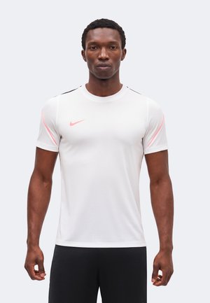 Homme athlétique portant un maillot de sport blanc à manches courtes avec des accents roses et un logo Nike rose, debout devant un fond uni.