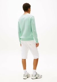 Mintgrüner Pullover, weiße Shorts, Sneakers aus Mischgewebe. Der Pullover hat gerippte Bündchen, die Shorts haben ein sichtbares Markenschild auf der hinteren Tasche.