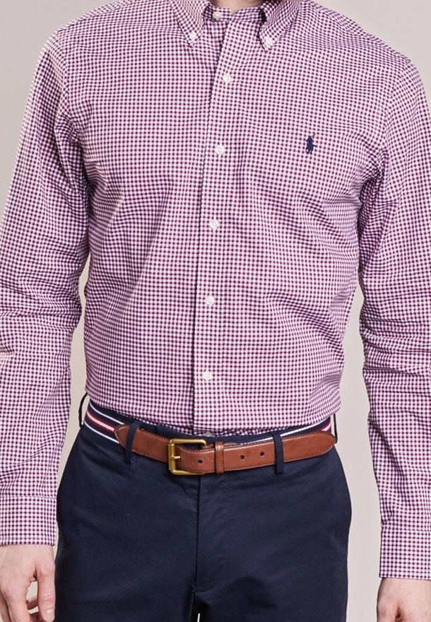 Röd och marinrutigt skjorta med knappad krage, långa ärmar och en liten logotyp, matchad med marinblå byxor och ett brunt bälte.