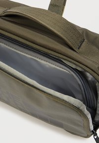 Πράσινη υφασμάτινη τσάντα με υφή στην εξωτερική επιφάνεια, διαθέτει κύριο διαμέρισμα και γκρι εσωτερική επένδυση. Περιλαμβάνει φερμουάρ και επιπλέον θήκη.