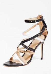 Musta, valkoinen ja beige korkokenkä, jossa on useita hihnoja ja solkia. Ominaisuuksiin kuuluu teksturoitu pinta ja teräväkärkinen muotoilu.