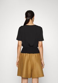 Top corto negro de manga corta con cintura fruncida; combinado con pantalones cortos de mezcla de lana marrón de textura suave y corte relajado.