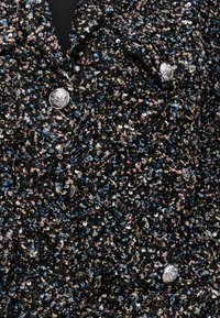 Tissu noir orné de petits sequins multicolores avec des accents bleus, roses et dorés ; détail de bouton argenté au niveau de la poitrine.