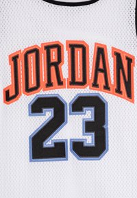 Valkoinen verkkopaita, jossa on oranssilla ja mustalla kirjoitettu "JORDAN" numeron "23" yläpuolella mustalla ja vaaleansinisellä, mustalla raidoituksella.