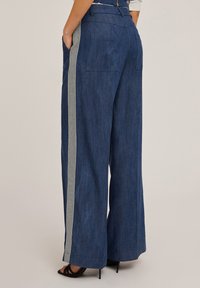 Tummansiniset leveälahkeiset farkut pystysuorilla raidoilla. Varustettu sivutaskuilla ja sileällä tekstuurilla. Takataskut näkyvissä.