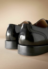 Zwarte patenten leren schoenen met textuurdetails, ronde hakken en gladde oppervlakken. Kenmerkt zich door contrasterende stiksels en een elegante uitstraling.