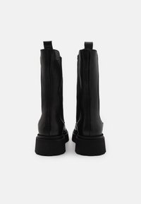 Botines de cuero negro con una textura suave, paneles laterales elásticos y una suela gruesa y robusta. Incluyen tiradores en la parte trasera.
