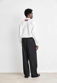 White long-sleeve shirt with a red accent at the back, paired with loose-fitting black pants. Smooth fabric, relaxed silhouette.