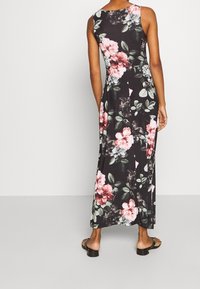 Robe longue florale présentant un fond noir avec des fleurs roses et blanches, un design sans manches et une silhouette fluide.