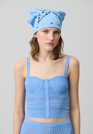 Top corto azzurro chiaro con texture a costine, chiusura con bottoni sul davanti e spalline sottili. Il foulard presenta disegni ritagliati e occhielli.