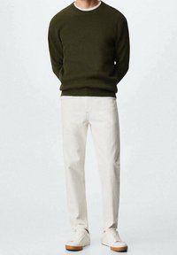 Pull texturé vert olive, sous-vêtement blanc, pantalon couleur crème, et baskets blanches avec semelles beige. Design simple, coupe ajustée.