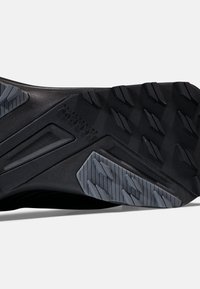 Schwarze Sportschuhsohle mit strukturiertem Gummiprofil, das ein graues Akzentmuster und verstärkte Traktionselemente für Stabilität aufweist.