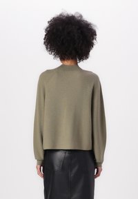 Khaki sweater with a crew neck, relaxed fit, and long raglan sleeves; paired with a black leather skirt featuring two back pockets.