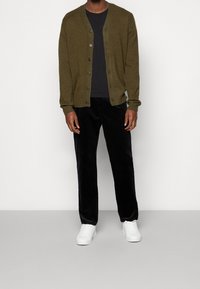 Olivgrön cardigan med v-ringning, långa ärmar och sexknäpps framknäppning, matchad med svarta velourbyxor och vita sneakers.