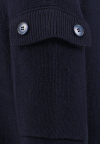 Marineblauer gestrickter Pullover mit einem gerollten Bund und zwei dunklen Knöpfen, der einen strukturierten Stoff mit einem einheitlichen Muster zeigt.