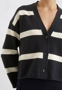 Schwarz-weiße gestreifte Strickjacke mit V-Ausschnitt, langen Ärmeln und fünf schwarzen Knöpfen vorne. Stricktextur mit verkürztem Design.