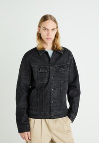 Black denim jacket with two chest pockets, button closure, and a structured design. Features stitched detailing and a casual fit.