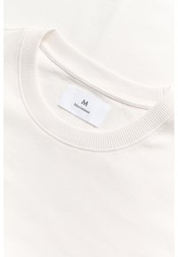 Samtbeiger Pullover mit geripptem Rundhalsausschnitt. Mit einem Etikett mit dem Schriftzug "Martinique" in schwarzer Schrift. Glatte Textur, minimalistisches Design.