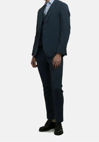 Marineblauw op maat gemaakt pak met een gelapte revers, zakdetails, slim-fit broek, gecombineerd met zwarte veterschoenen. Soepele stofstructuur.