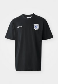 Fekete, rövid ujjú pamut póló, kerek nyakkal. Fehér Adidas logóval és egy kék emblémás folttal a bal mellkasán.