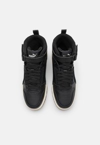 Wysokie sneakersy z czarną skórzaną cholewką, teksturowanymi detalami, wyściełanym kołnierzem i regulowanym paskiem. Biała podeszwa stanowi kontrast.