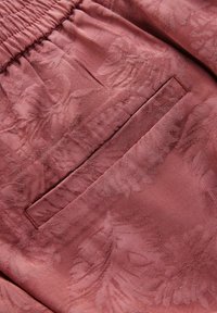 Rosa tyg med ett subtilt blommönster, med en rynkad midja och en diskret ficka på sidan. Mjuk textur.