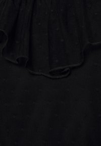 Tessuto nero strutturato con pois in rilievo e morbide rouches lungo il bordo superiore, creando un aspetto stratificato.