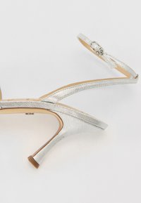 Silver high-heeled sandals with textured straps and a thin ankle strap, featuring a sleek design and a narrow pointed toe.