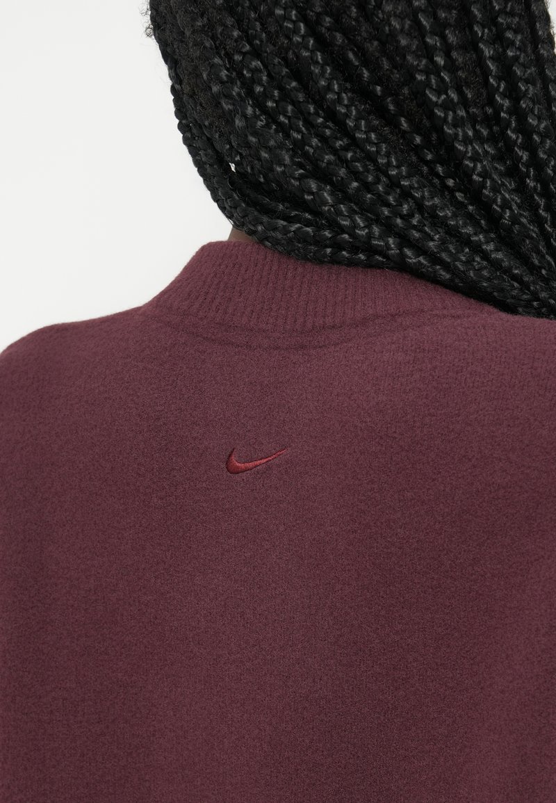 Burgundy Nike sweatshirt har en hög krage och mjuk textur, med en liten broderad logotyp på baksidan i matchande burgund.