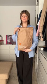 Brown paper bag with text "Love me. Wear me." in white and orange. Model wearing a light blue shirt and dark pants, holding the bag.