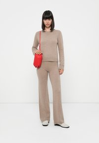 Beige gebreide trui en bijpassende flared broek, aangevuld met een rode tas. Zachte textuur, aansluitend ontwerp, gezellige en informele uitstraling.