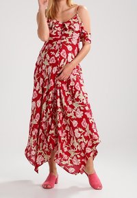 Rode maxi-jurk met bloemenprint en off-shoulder mouwen, met lichtgele bloemmotieven, een vloeiende silhouet en een high-low zoom. Gecombineerd met roze mules.