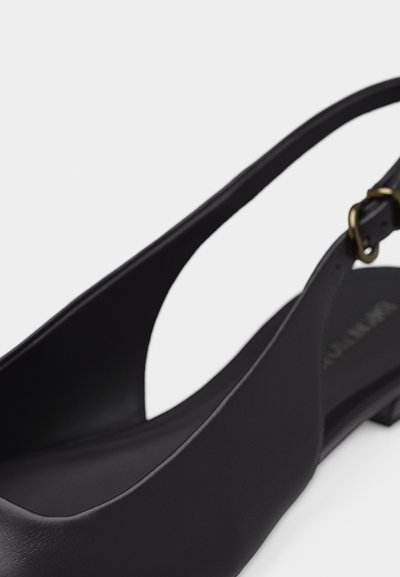 Μαύρο δερμάτινο φλατ παπούτσι slingback με χρυσή αγκράφα και στρογγυλεμένη μύτη, απεικονιζόμενο από κοντινή γωνία.