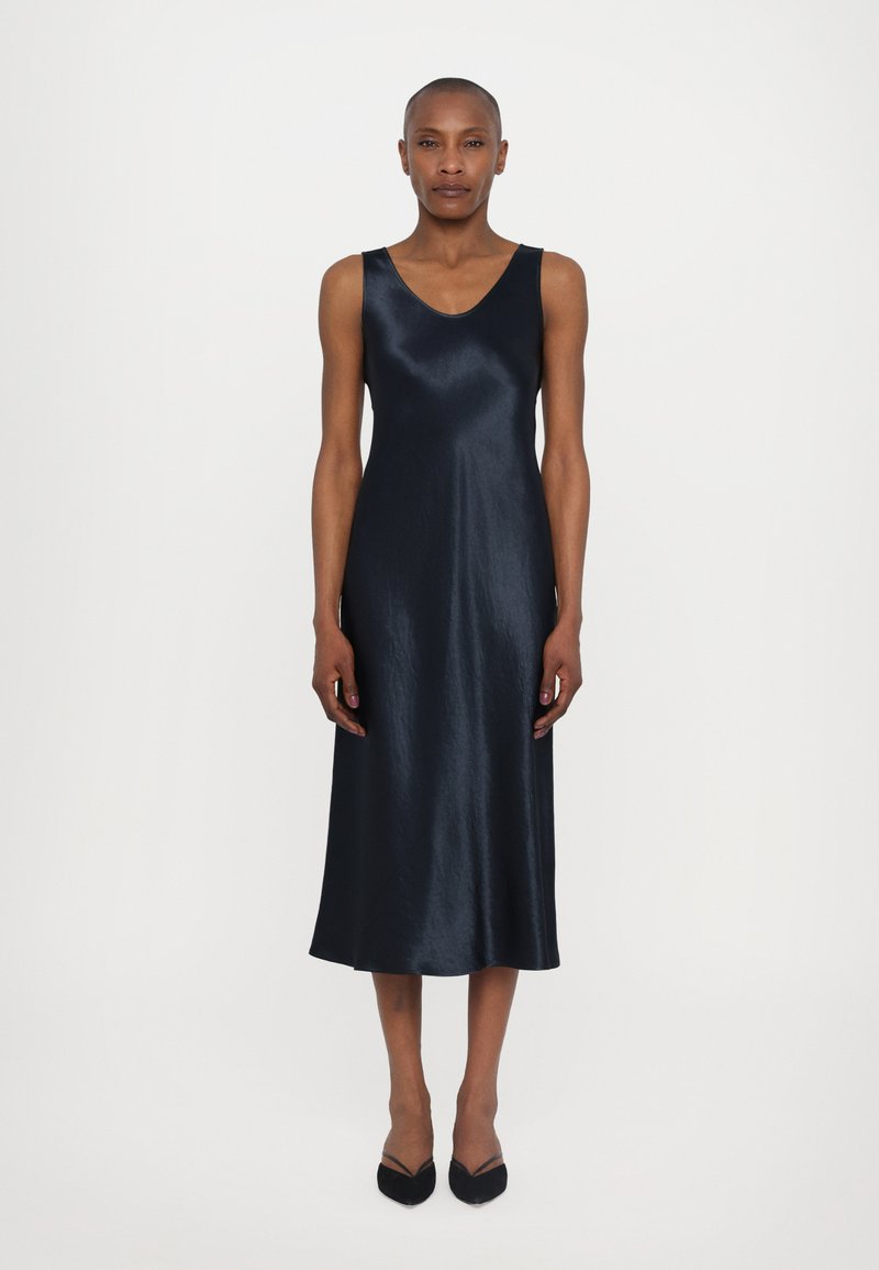 Robe sans manches en satin marine avec un décolleté en V, silhouette en A, texture lisse et ourlet au genou. Associée à des chaussures noires à bout pointu.