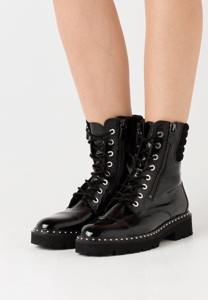 Bottes de combat en cuir verni noir avec laçage sur le devant, fermeture éclair latérale, détails cloutés le long de la semelle et accents texturés en haut.