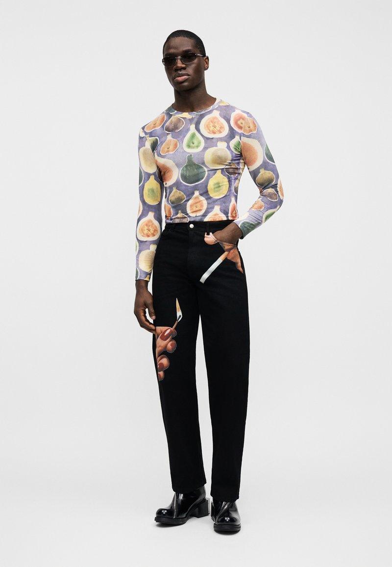 Tričko s dlhým rukávom s potlačou ovocia v pastelových farbách na sivom pozadí; v páre s čiernymi nohavicami s grafikou ruky a nožníc.