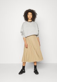 Felpa grigia con spalle scese, abbinata a una gonna midi plissettata beige. Sneakers nere con dettagli viola completano l'outfit.